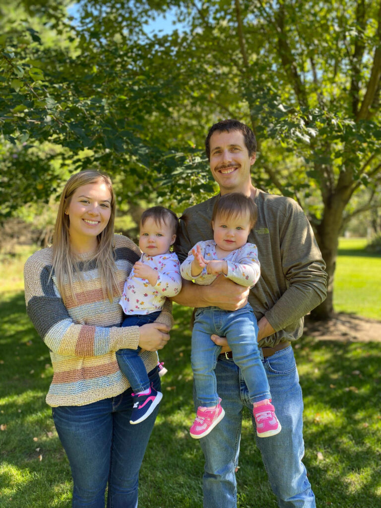 parents standing by tree each hold a toddler
